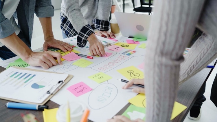 Close crop of three people in business casual clothes making notes and arranging Post-Its on a desk top