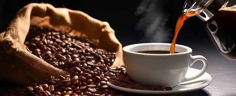 steaming mug of coffee next to overflowing bag of coffee beans