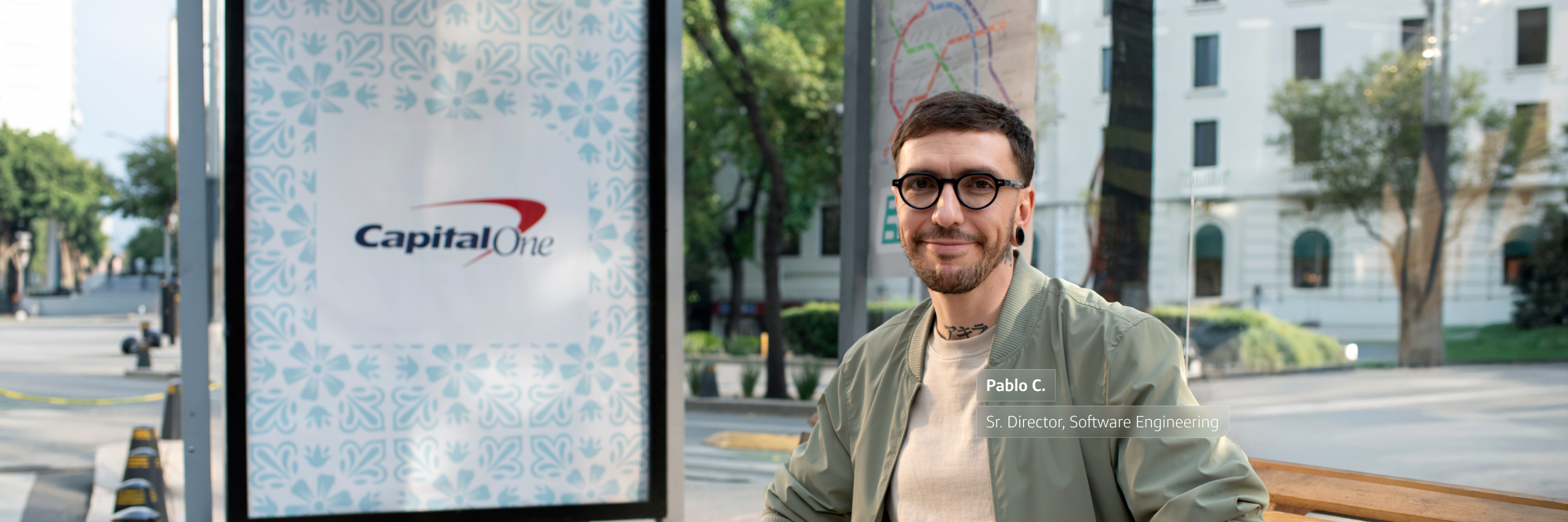 Pablo C. - Senior Director, Software Engineering, sits at bus stop with Capital One ad in background