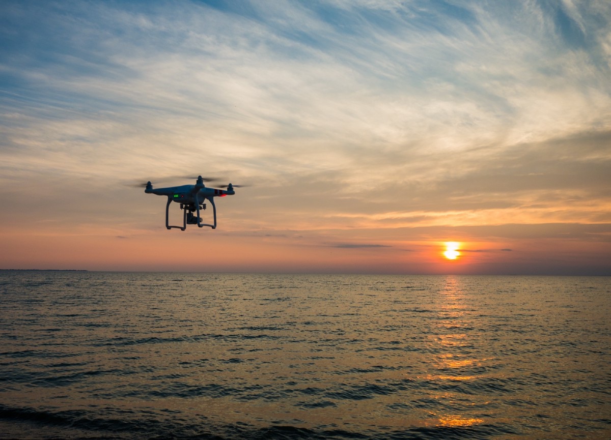 black drone flying over ocean with sun setting on horizon in distance