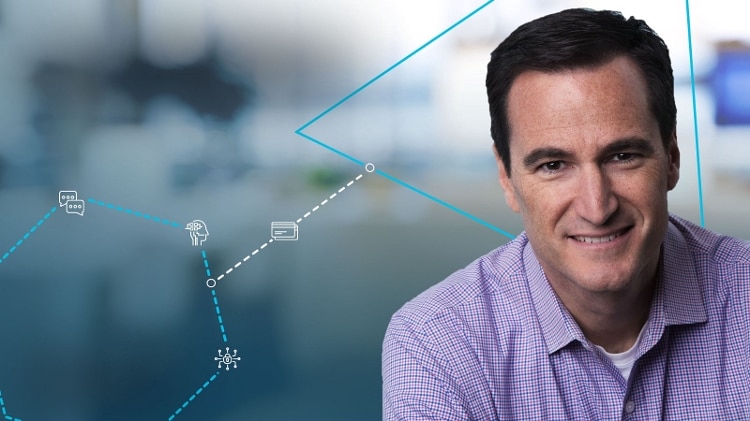 man smiling, wearing pink and blue plaid shirt with thin lines, with blurred background and blue lines making hexagon and triangle. white icons connect the 2 shapes