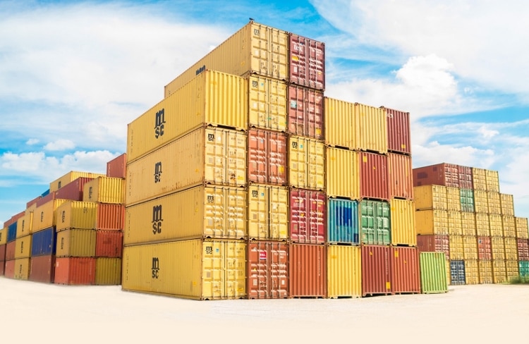 yellow, orange, red, blue, and green shipping containers stacked in a pile towards a blue sky