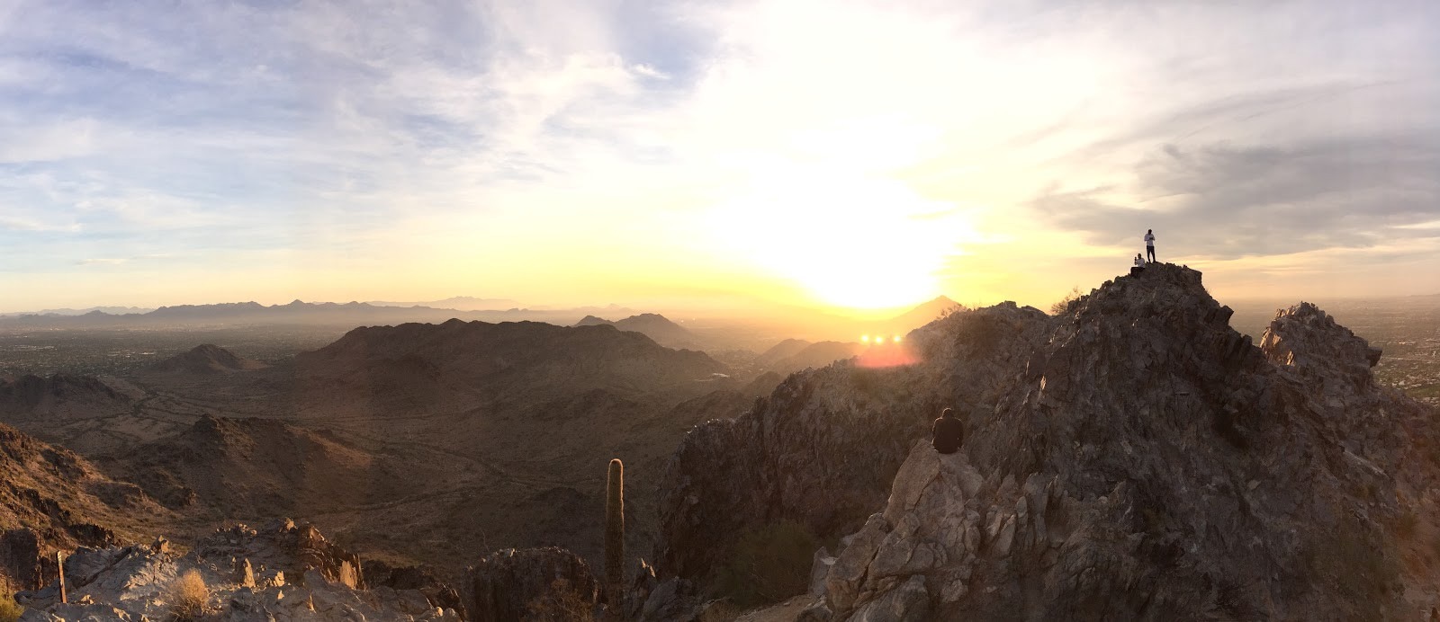 large mountain rock peaks with man standing on highest one, with sun shining in background