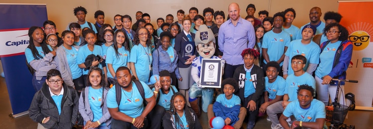 group of students and teachers wearing blue tshirts, posing with cowboy mascot holding a navy and white framed certificate
