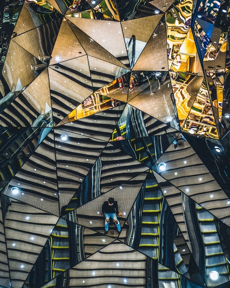 triangular mirrors making up abstract 3d hexagonal design, and man in blue shirt reflected in the middle