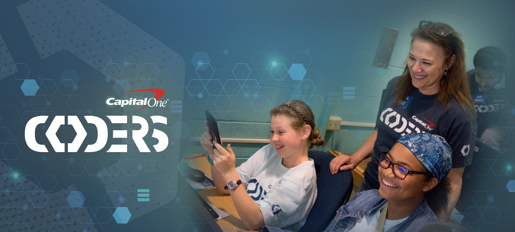 female capital one associate wearing navy shirt mentoring 2 younger girls holding black tablets. there is a navy overlay with blue and white hexagons and coders logo