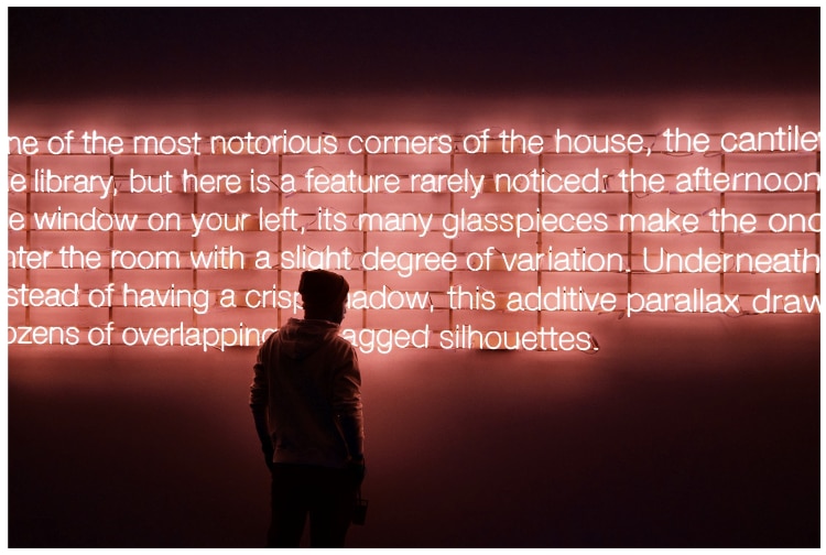 dark figure looking at a wall of white neon text with red backlight.