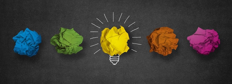 blackboard with 5 crumbled up pieces of paper - blue, green, yellow, orange, and pink. yellow one in center has white chalk lines around it to create a lightbulb
