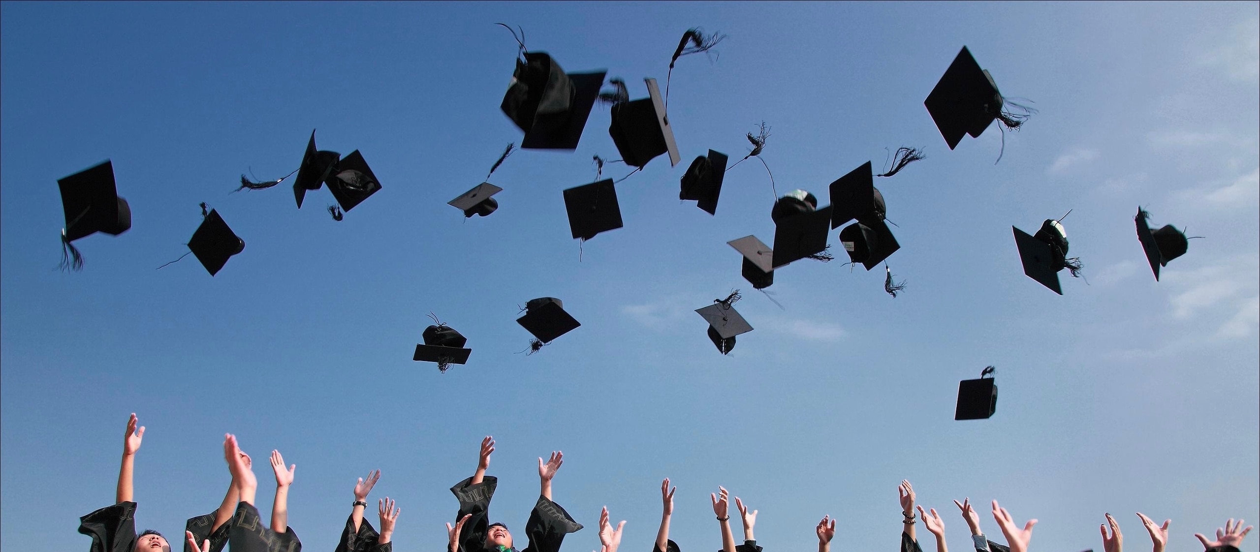 blue sky with many black graduation caps scattered, as if they were just tossed in the air