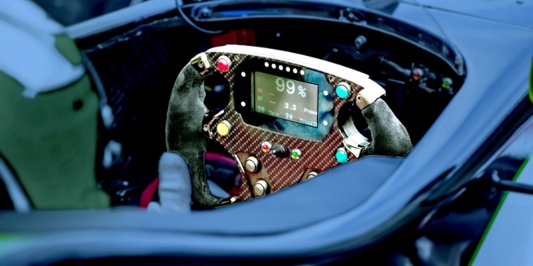 racecar steering wheel with brown metal plate, green, red, and yellow buttons, and green screen reading "99%" in white