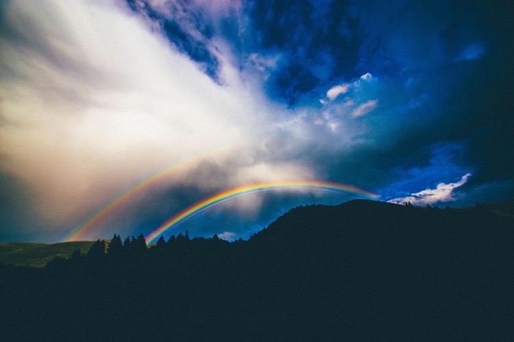 rainbow arching over mountains, with blue sky and sunshine