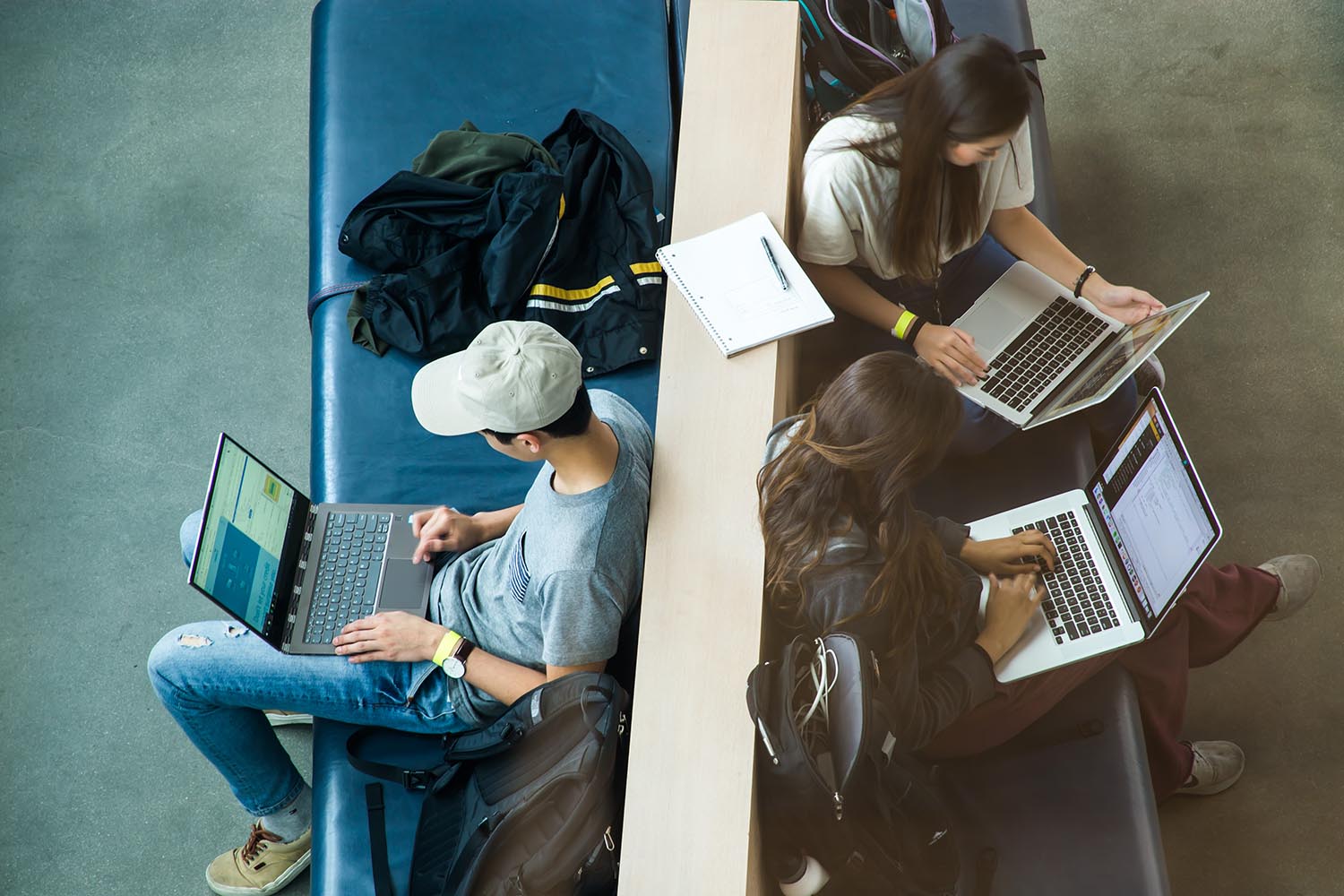 aerial shot of developers sitting on blue bench with open silver laptops with black keyboards.