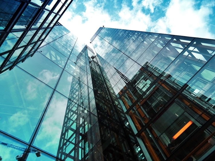 sky scrapers with clear windows going up towards a blue sky with bright sun
