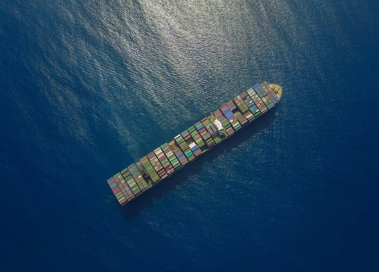 aerial shot of blue ocean with large, long boat carrying many green, blue, red, yellow, white, and brown shipping containers