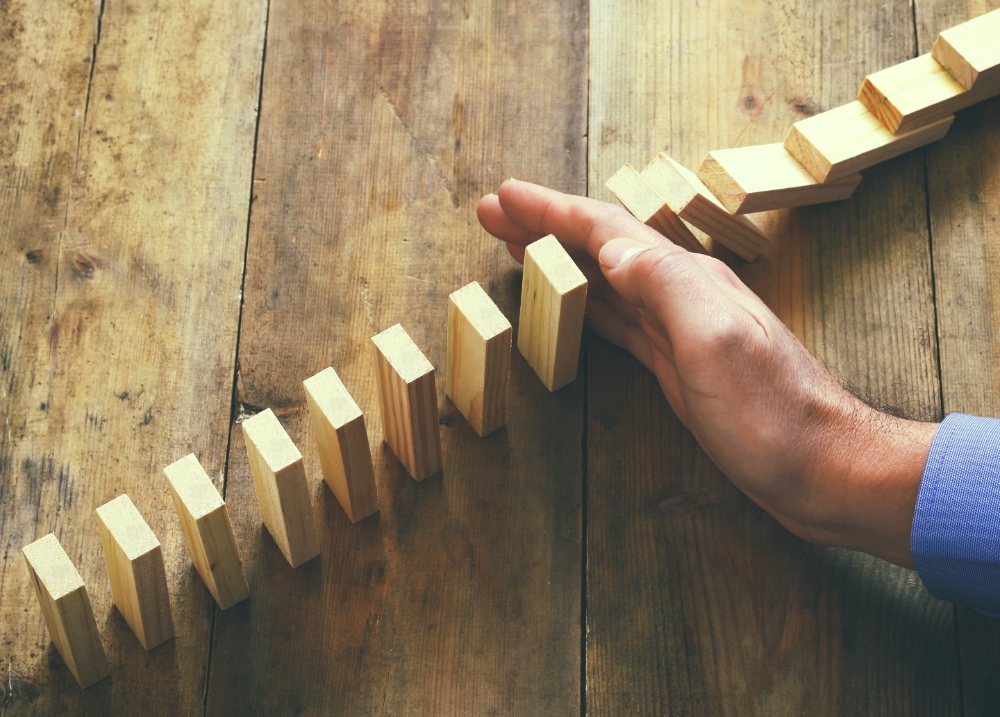 light brown rectangular blocks standing up, arranged in a line. someone's hand with a shirt blue sleeve is coming between them as if it were about to knock them over