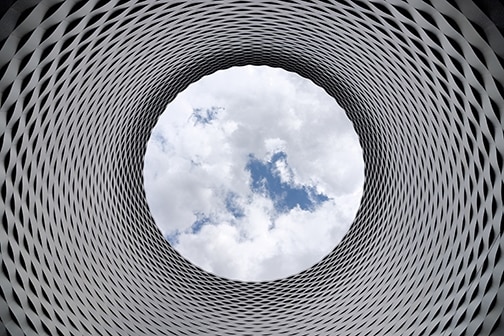 white pipe with repeating black triangles, with cloudy blue sky at the other end