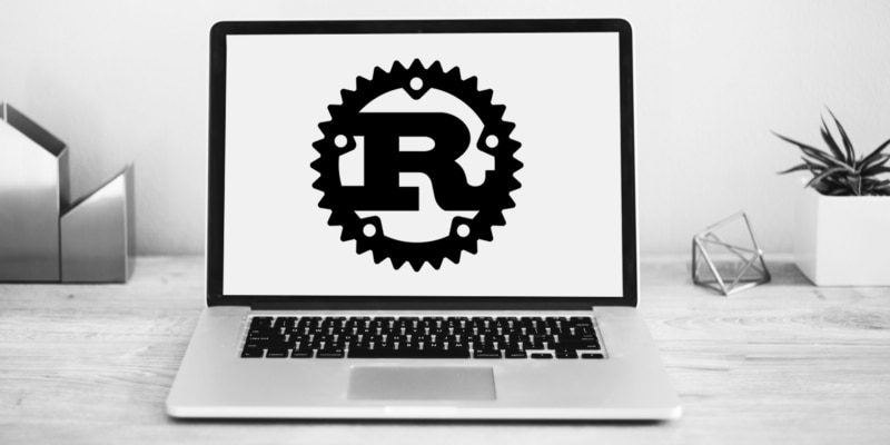 greyscale photo of laptop sitting on table with white screen with large black gear with black "R" in the middle