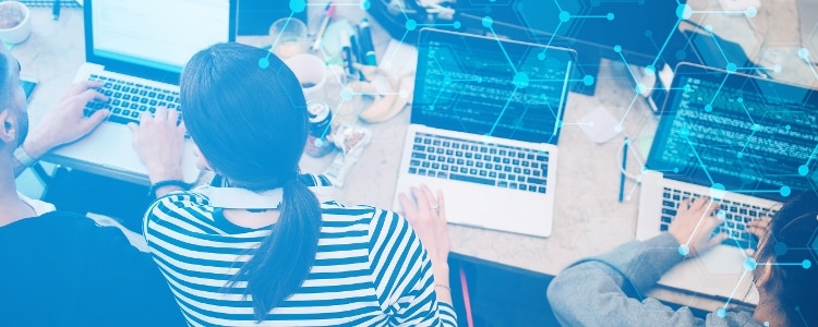 aerial shot of woman in striped black and white shirt sitting next to man in black shirt and woman in grey sweatshirt. all 3 have their silver laptops open to black screen with lines of white code on them. there is a light blue gradient treatment and blue and white lines and dots overlaid on the whole image.