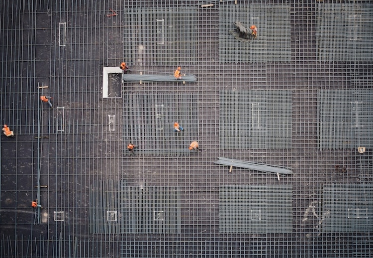 aerial shot of construction workers in orange vests working on grid of silver pipelines
