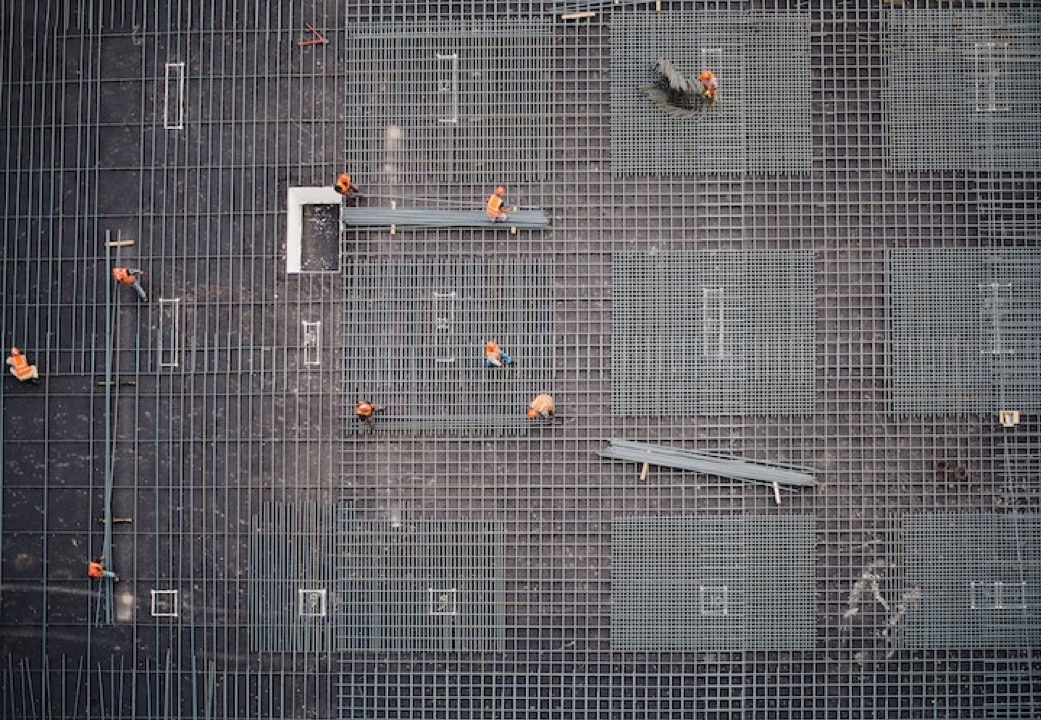 aerial shot of construction workers in orange vests working on grid of silver pipelines