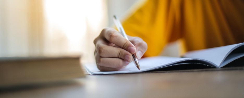 close up shot of womans hand holding pen and writing in notebook
